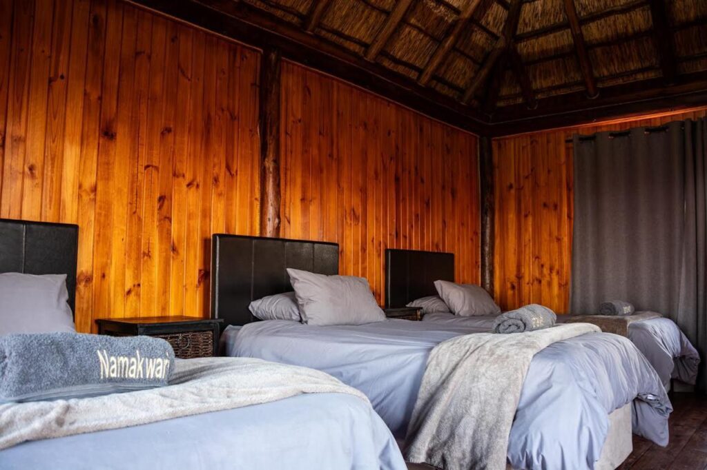 Spacious bedroom at Namakwari hunting lodge in Kalahari featuring double beds and rustic charm