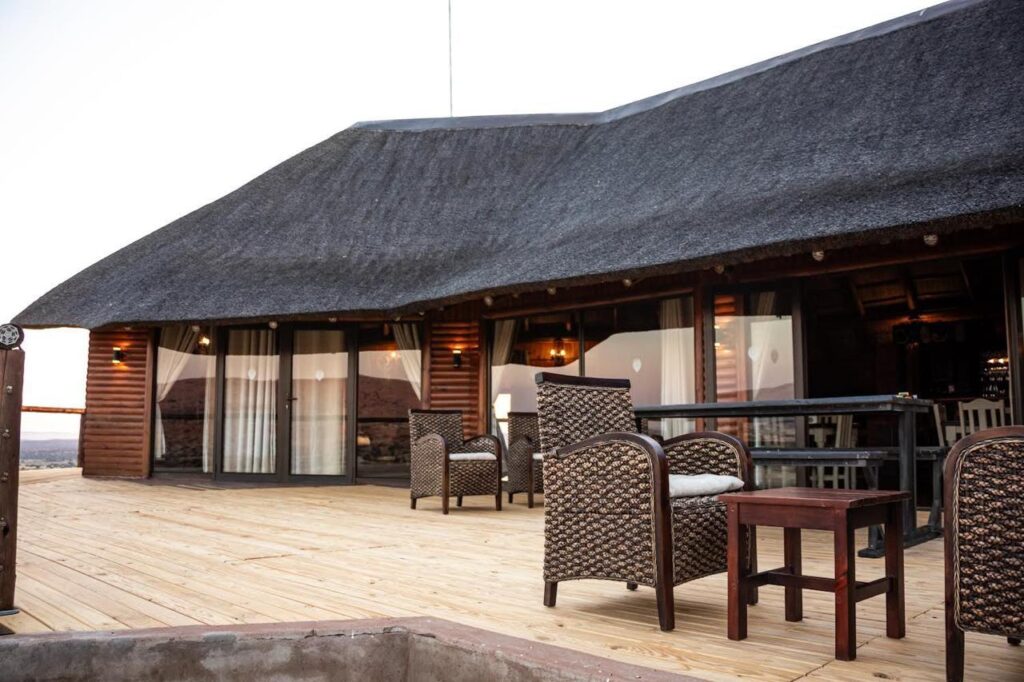 Thatched-roof lodge exterior with cozy seating at Namakwari hunting lodge in Kalahari