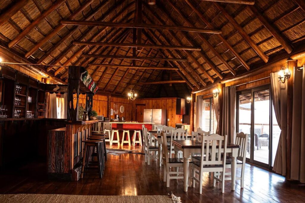 Thatched-roof dining area at Kalahari hunting lodge with rustic wooden furniture and bar